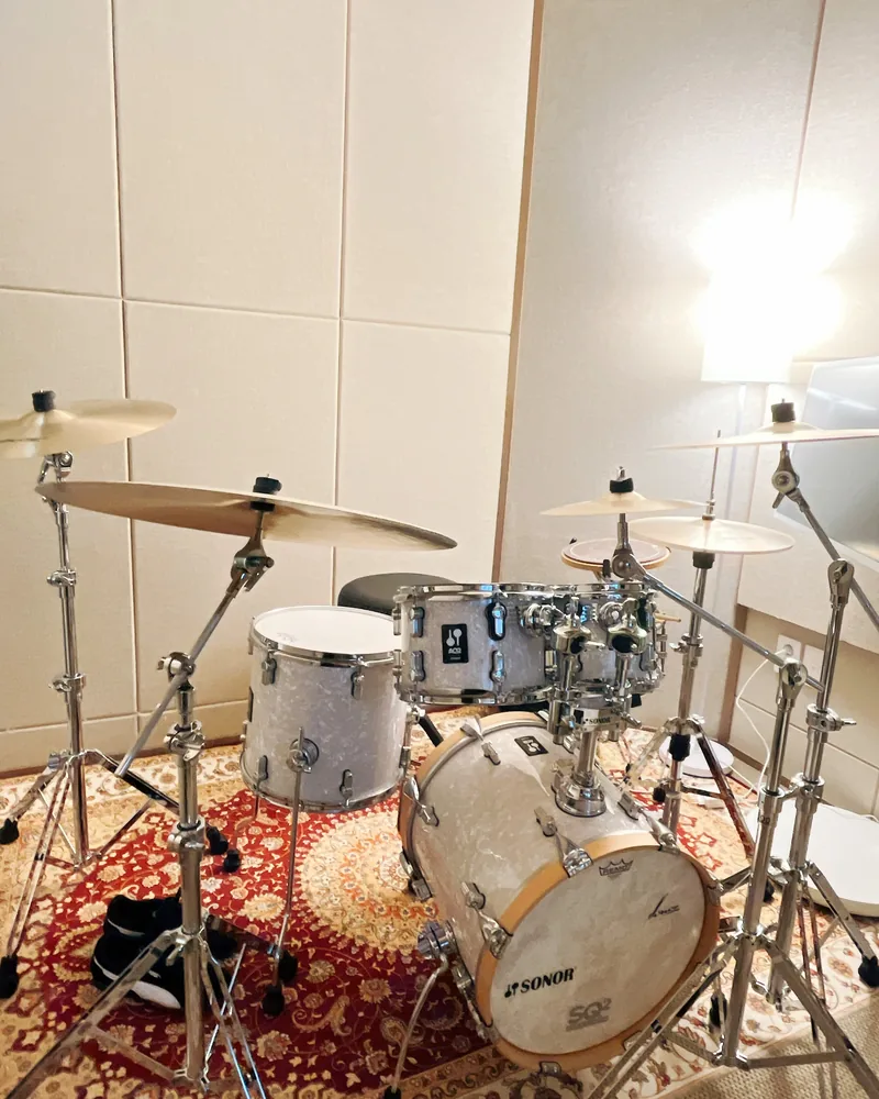 A practice room at Drum Avenue with a white drum kit on a patterned rug and a floor lamp / 무늬 러그 위에 흰색 드럼과 스탠드 조명이 있는 드럼에비뉴 연습실